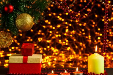 Noel ağacı dalının köşesindeki altın çelenklerin Bokeh Noel arkaplanı. Noel ağacı kutularının altında parlak bir top ve cam bir mumla..