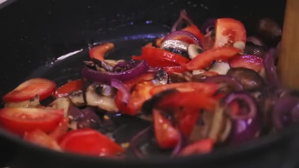 У сковороді з грибами та цибулею рука змішує помідори з шпателем — стокове відео