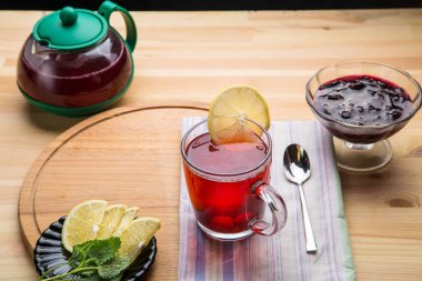 Çaydanlık kaşığı, limon ve limon merheminin yanında bir fincanda çilek çayı ve peçete..