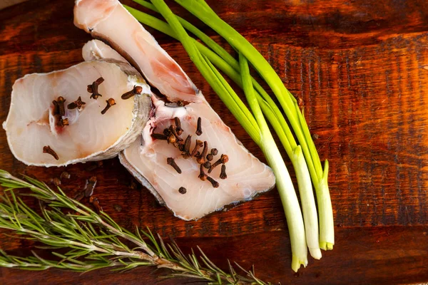 Biberiye ve soğanın yanına baharat serpiştirilmiş tahtadan yapılmış taze balık biftekleri.. — Stok fotoğraf