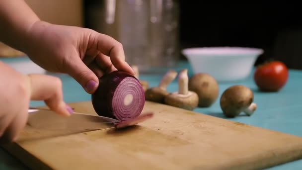 Una mano femminile su una tavola di legno taglia una cipolla rossa in anelli. — Video Stock