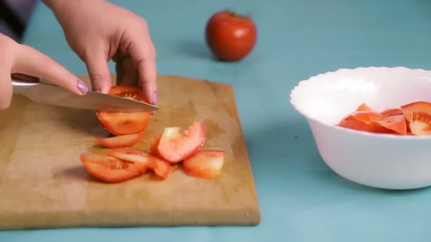 Una mano femenina sobre una tabla de madera corta tomates rojos con un cuchillo — Vídeos de Stock