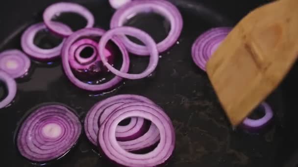 A womans hand mixes a red onion in a frying pan with a wooden spatula. — Stock Video