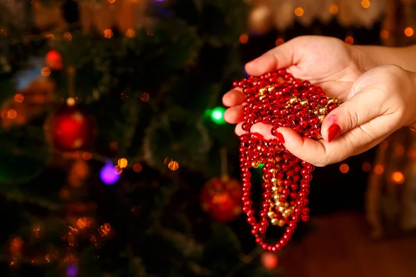 Kerst decoraties van een ketting in vrouwelijke handen op de achtergrond van een kerstboom. — Stockfoto