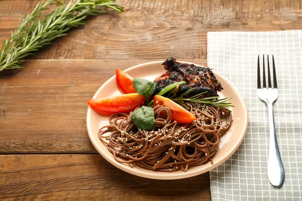 Een bord soba met kiptomaten en spinazie op een linnen servet naast een vork op de tafel. — Stockfoto