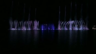Gece gökyüzünün arka planında farklı kombinasyonlarla su üzerinde çok renkli fıskiyeler.