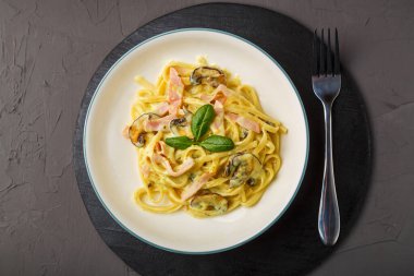 Kremalı fesleğen sosunda jambonlu ve mantarlı bir tabak makarna siyah yuvarlak bir büfede çatalla..