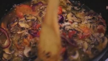 Mantar ve soğanlı bir tavada, domates ve pirinç bir spatulayla karıştırılır..