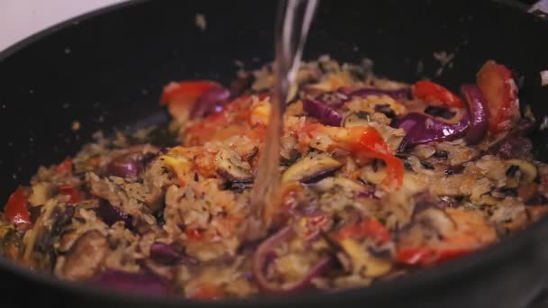 Woda jest wlewana do patelni risotto z grzybami i cebulą, pomidorami i ryżem. — Wideo stockowe