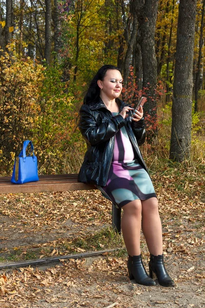 去年秋天，在公园长椅上怀孕的黑发女人用智能手机看书. — 图库照片