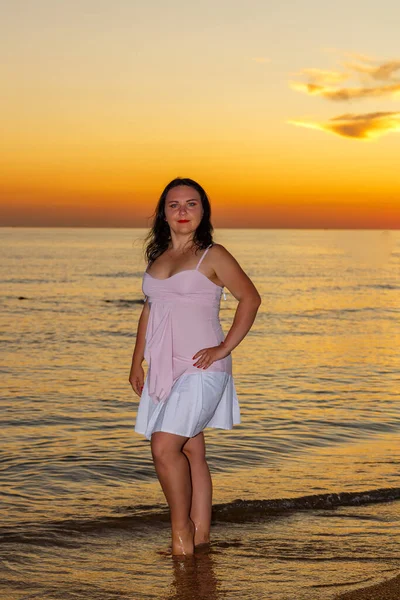Молодая женщина в белом платье стоит на берегу моря на закате. — стоковое фото