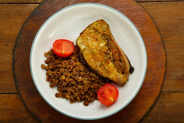 A plate of fish with lentils and tomatoes on a wooden table. — Stock Photo, Image