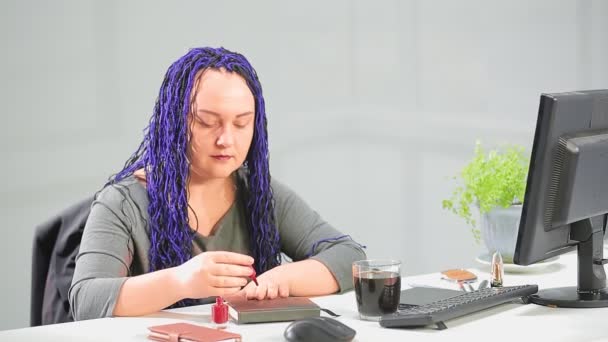 Kobieta w biurze z niebieską afro-fryzurę maluje paznokcie z jasnoczerwonym lakierem — Wideo stockowe