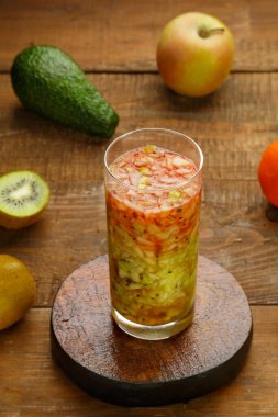 Elmalı kivi kokteylinin yanında, ahşap bir masanın üzerinde bir bardak kivi kokteyli. Dikey fotoğraf