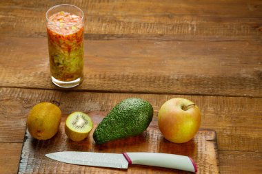 Bir bardak kivi elmalı kokteyl. Tahta bir masanın üzerinde. Elmalı avokado ve bıçağın yanında. Yatay fotoğraf.