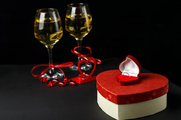 Şampanyalı bardaklar, hediye ve yüzükle dolu kalp şeklinde siyah arka plan kutularına kurdele bağlanmış. Yatay fotoğraf.