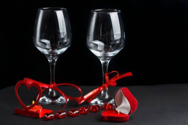 Siyah arka planda iki şampanya bardağı, kalp şeklinde bir kutunun yanında bir yüzük ve bir ayçiçeği..