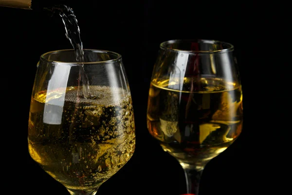 Champagne is poured into glasses without legs on a black background.