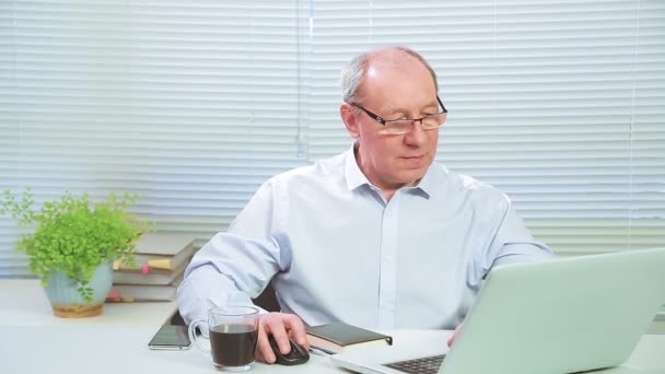 Executivo masculino em óculos no escritório no computador trabalha perto de um bloco de notas e café — Vídeo de Stock