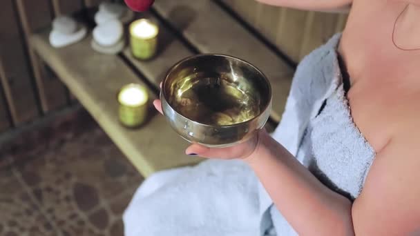 Den sjungande skålen gör ljud i händerna på en ansiktslös kvinna på ett spa — Stockvideo