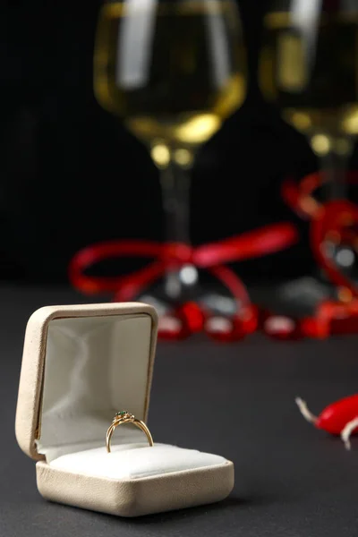 On a black background, a box with a ring in the background glasses of champagne and souvenirs out of focus. Vertical photo