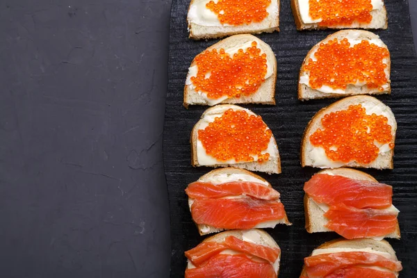 Kırmızı havyarlı ve alabalıklı sigara gri beton arka plan fotokopi alanındaki siyah tahtaya serilmiş. Dikey fotoğraf