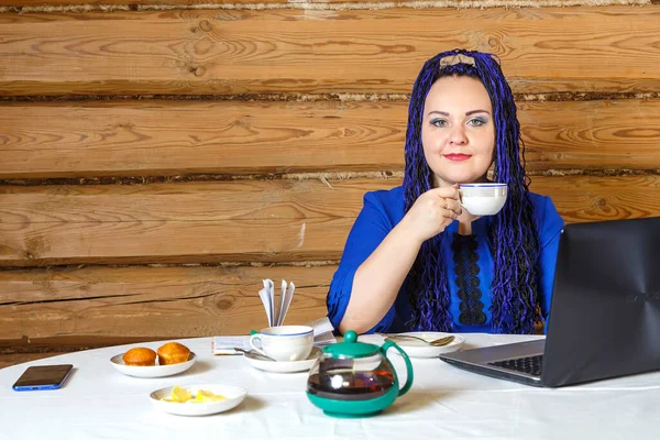 Жінка з блакитними косами в домашньому офісі за комп'ютером працює і п'є чай . — стокове фото