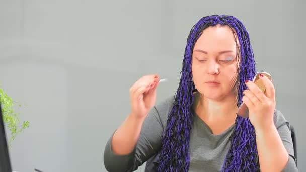 Židovka v kanceláři s modrým afro-účesem maluje oči se stíny, dívá se do malého zrcadla — Stock video