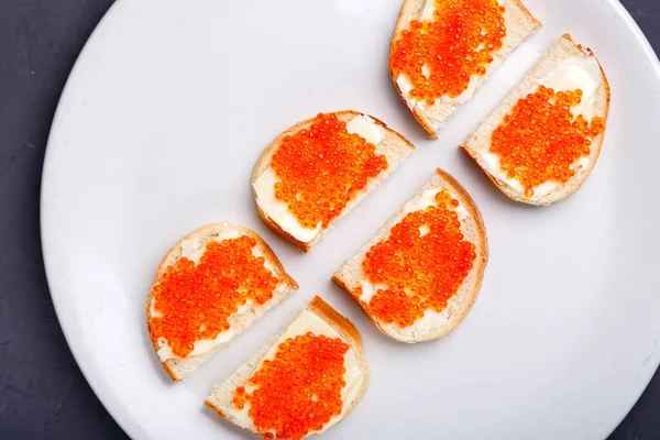 Brosses avec beurre et caviar rouge sur une assiette blanche disposée sur un fond de béton gris. Espace de copie. — Photo
