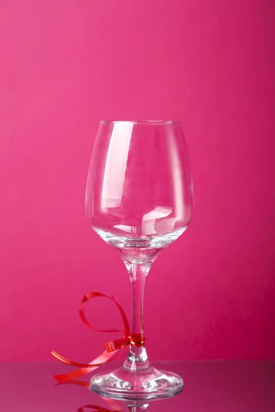 Copo de champanhe com fita vermelha em um fundo rosa. — Fotografia de Stock