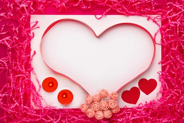 Em um fundo rosa, um coração volumétrico feito de papel e seixos e fitas e rosa decoração de rosas. — Fotografia de Stock