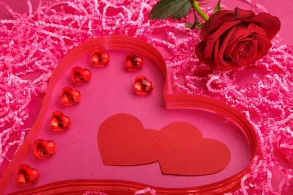 On a pink background, a fragment of a volumetric heart made of paper and pebbles and ribbons, and next to a rose. — Stock Photo, Image