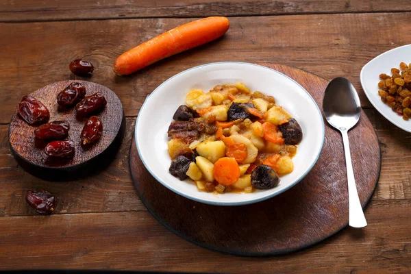 Bir tabak yahudi mutfağı - havuçlu tsimes ve yuvarlak bir tabakta bir kaşığın yanında beyaz bir tabakta hurma ve kurutulmuş meyveli havuçlar.