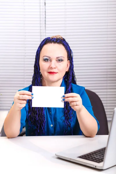 Μια γυναίκα στο γραφείο με μπλε Afro πλεξούδες στον υπολογιστή κρατά μια επαγγελματική κάρτα στα χέρια της. — Φωτογραφία Αρχείου