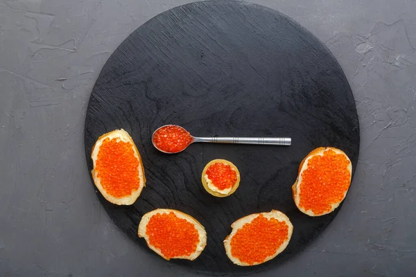 Tostada con mantequilla y caviar rojo junto a una cuchara con caviar sobre una tabla de madera sobre un fondo de hormigón. Copiar lugar. — Foto de Stock