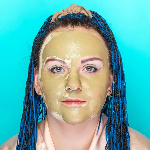 Жінка з блакитними косами обличчям в масці з зеленої глини на синьому фоні . — стокове фото