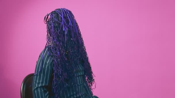 Eine stylische brünette Jüdin mit blauen Afro-Zöpfen auf einem Stuhl schüttelt effektiv ihre Haare und bedeckt ihr Gesicht. — Stockvideo