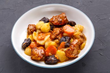 Bir tabak yahudi mutfağı havuç, hurma ve hindi eti ile beton bir arka planda beyaz bir tabakta.