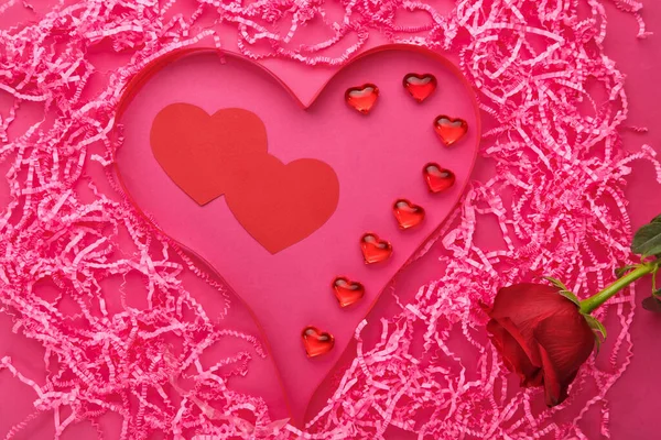 Op een roze achtergrond, decoratie voor Valentijnsdag een hart gemaakt van papier en steentjes in de buurt van een roos. — Stockfoto