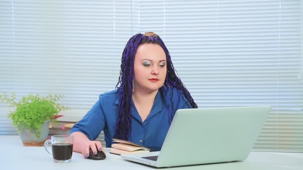 Ofiste mavi afro örgülü bir kadın elinde not defteriyle bilgisayar başında çalışıyor. — Stok video