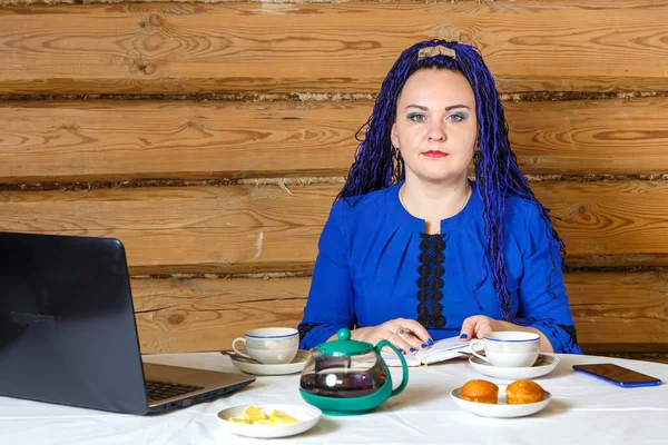 在电脑房的办公室里，一个头戴蓝色非洲式辫子的女人一边工作一边喝茶. — 图库照片