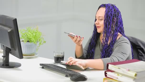 Vrouw in het kantoor met een blauwe afro kapsel werkt voor het communiceren op de luidspreker — Stockvideo