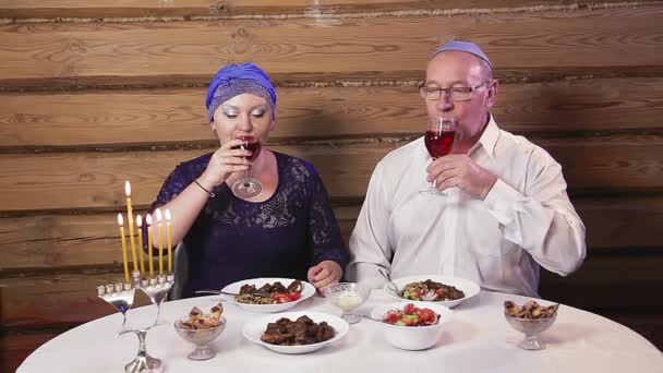 Єврейська пара в головному уборі чоловік у кіппі за столом зі свічками в дні обіду Хануки. — стокове відео