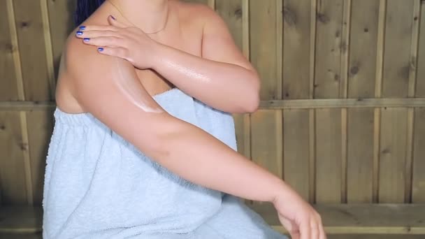 En kvinna slappnar av i ett spa bad i en handduk med blå afro flätor och applicerar lotion på huden — Stockvideo