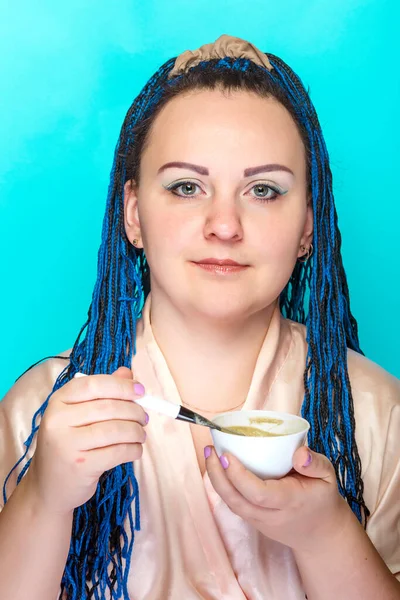 年轻女人手里拿着非洲辫子，用猪口刷在蓝色的背景上做口罩. — 图库照片