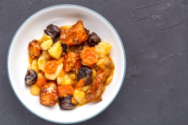 Bir tabak yahudi mutfağı havuç, hurma ve hindi eti ile beton bir arka planda beyaz bir tabakta.