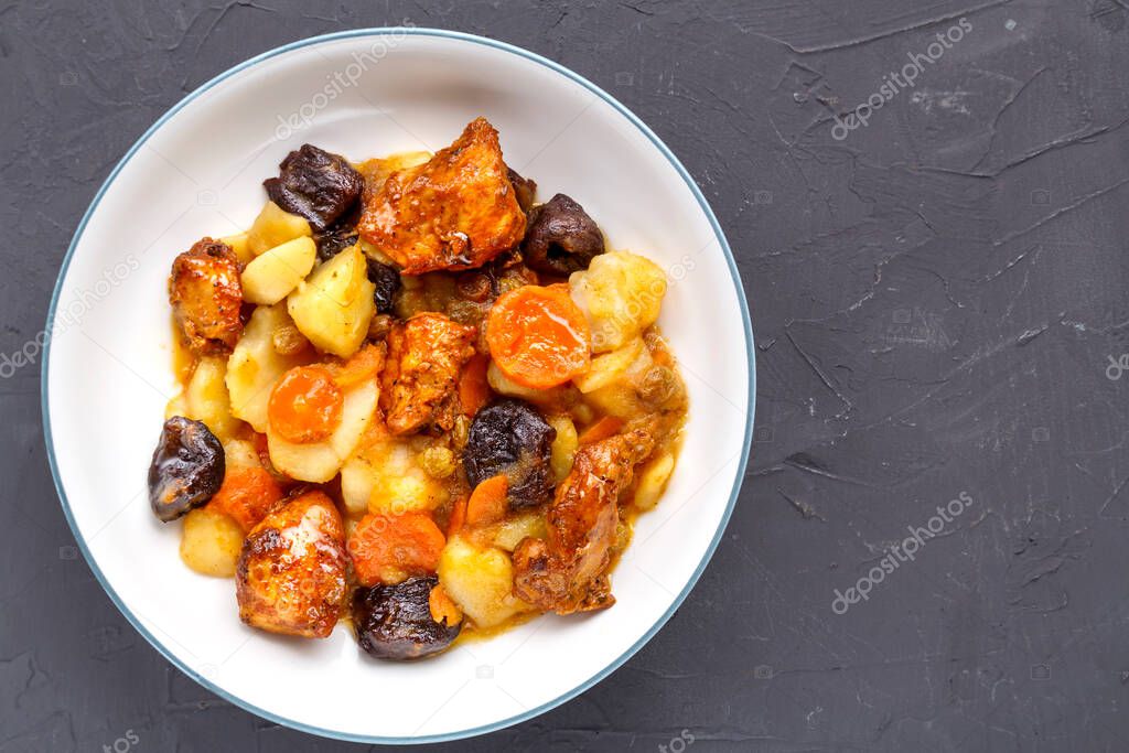 A dish of Jewish cuisine sweet tsimes with carrots, dates and turkey meat in a white plate on a concrete background.
