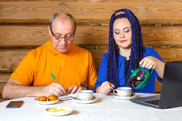 Сімейна пара чоловік в окулярах і жінка з блакитними косами за столом жінка п'є чай чоловік пише інформацію . — стокове фото