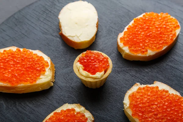 Canapés avec beurre et caviar rouge sur une planche noire sur un fond de béton. — Photo