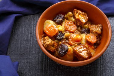 Mavi arka planda kahverengi bir tabakta hurma, havuç ve hindi eti bulunan yahudi mutfağı tatlısı.